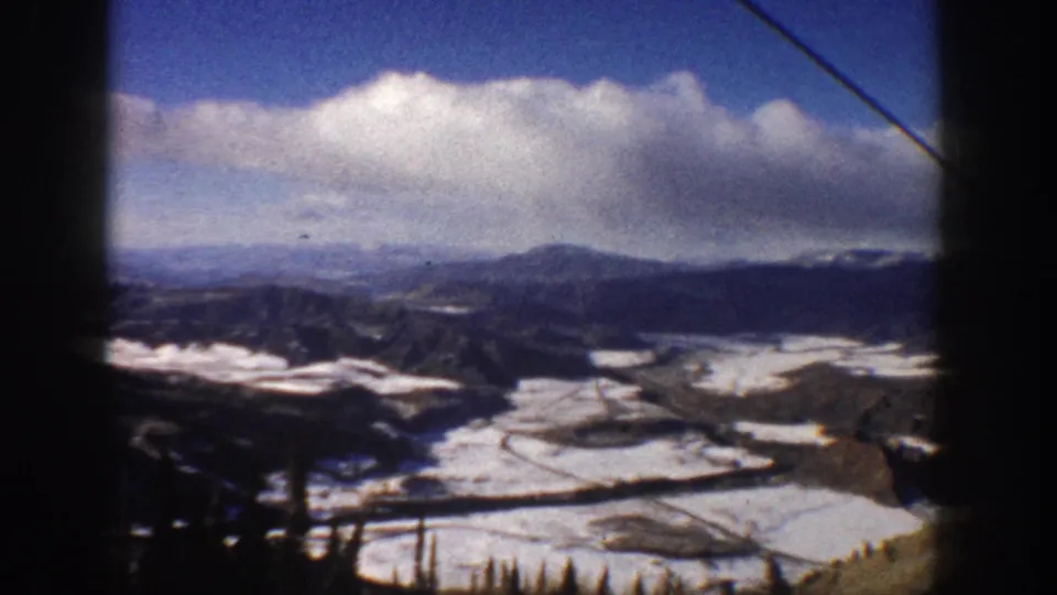 Moving 8mm view from a ski lift in Aspen, Colorado, showing snowy valley terrain, roads, and distant peaks.