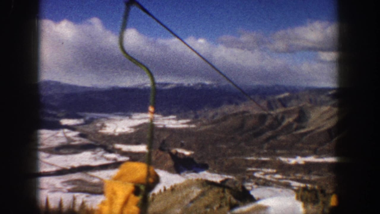 1961 Aspen ski-lift view across snow-dappled Colorado mountain slopes, with cables and yellow lift hardware in the foreground.