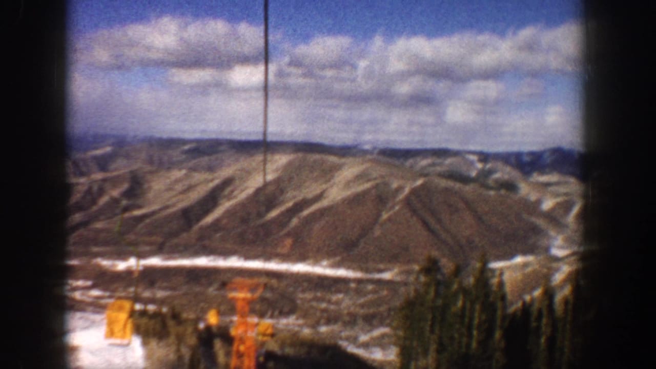 1961 Aspen-area 8mm view of snow-dusted Colorado mountain slopes and scattered clouds, with dark film-frame edges visible.