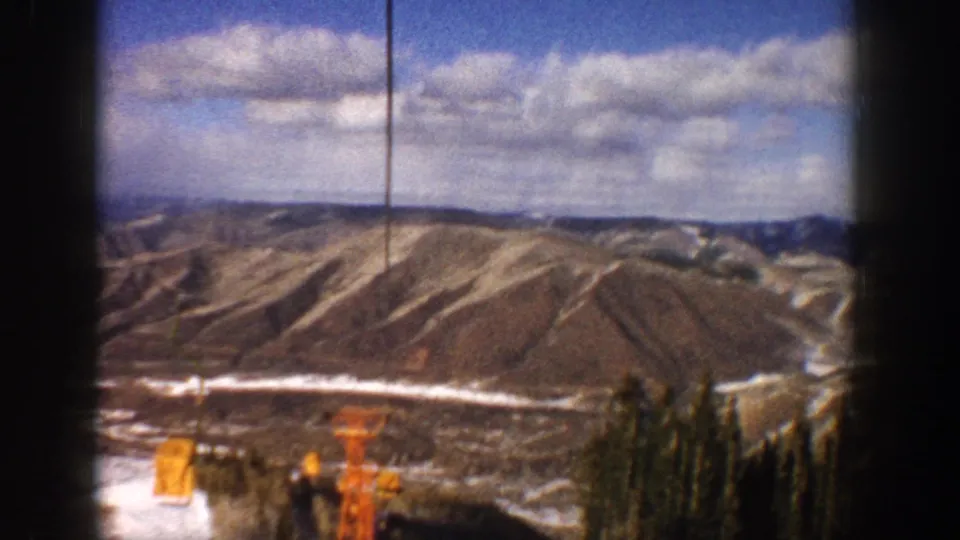 1961 Aspen-area 8mm view of snow-dusted Colorado mountain slopes and scattered clouds, with dark film-frame edges visible.
