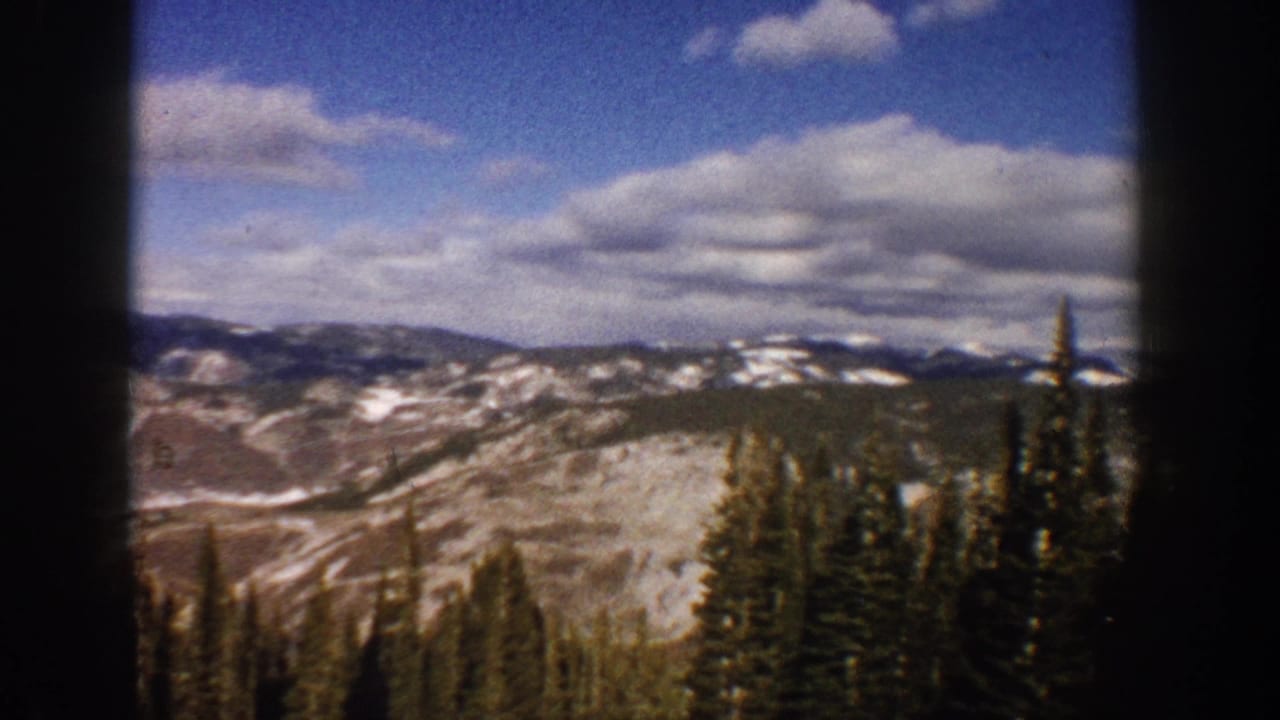 Aspen, Colorado 1961 home-movie view of snowy mountain ridges, evergreen trees, and a bright clouded sky.