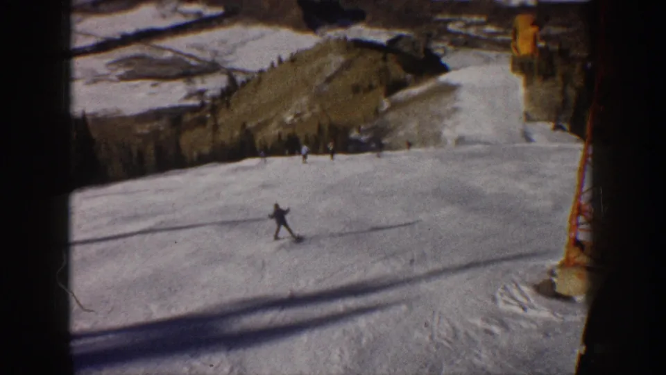 Distant skier descending an Aspen slope in 1961, with lift structure, snow texture, and wooded hills visible.