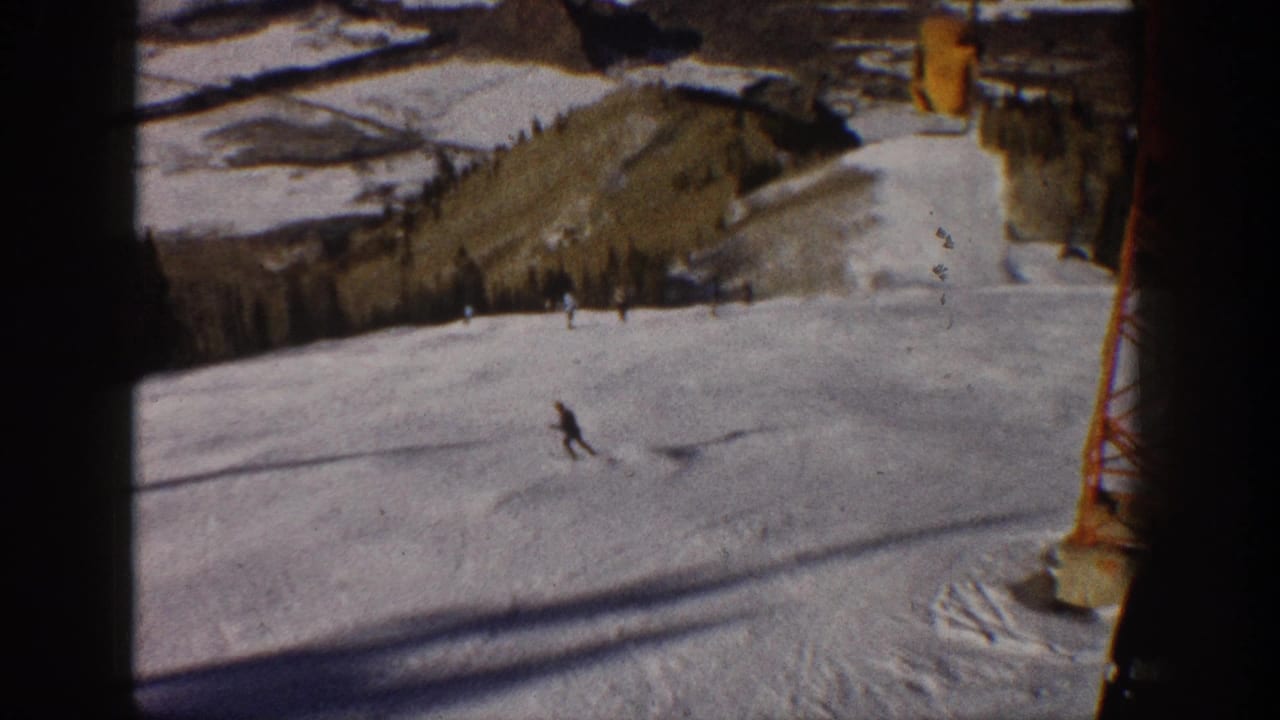1961 Aspen, Colorado home-movie frame showing a distant skier on a snowy run with a yellow lift tower and hills behind.
