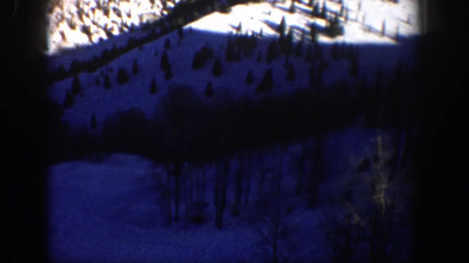 1961 Aspen-area 8mm frame showing a blue-toned snowy hillside with scattered conifers and bare trees.