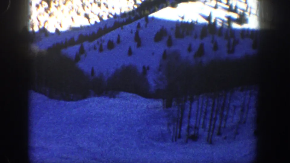 Aspen winter frame from 8mm footage showing a blue-hued snowy slope with conifers and bare aspen-like trees.
