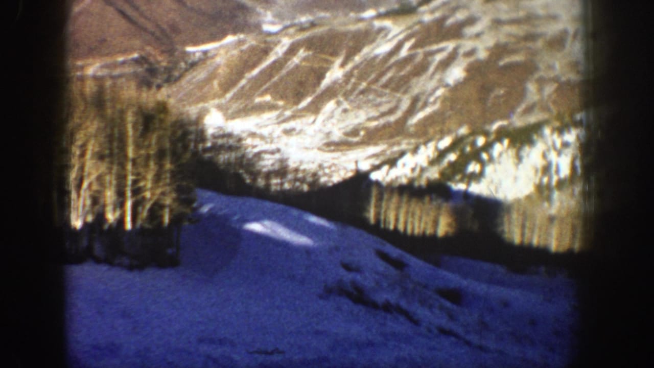 1961 Aspen, Colorado home-movie frame showing blue-tinted snow below bare trees and a distant sunlit mountain slope.