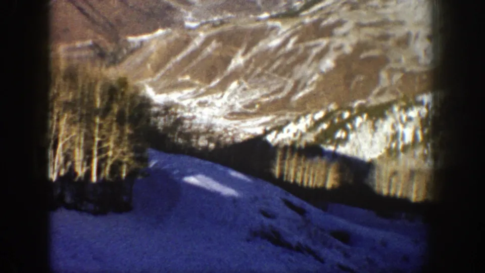 1961 Aspen, Colorado 8mm frame showing a snow-covered slope, sparse bare trees, and distant winter mountain terrain.