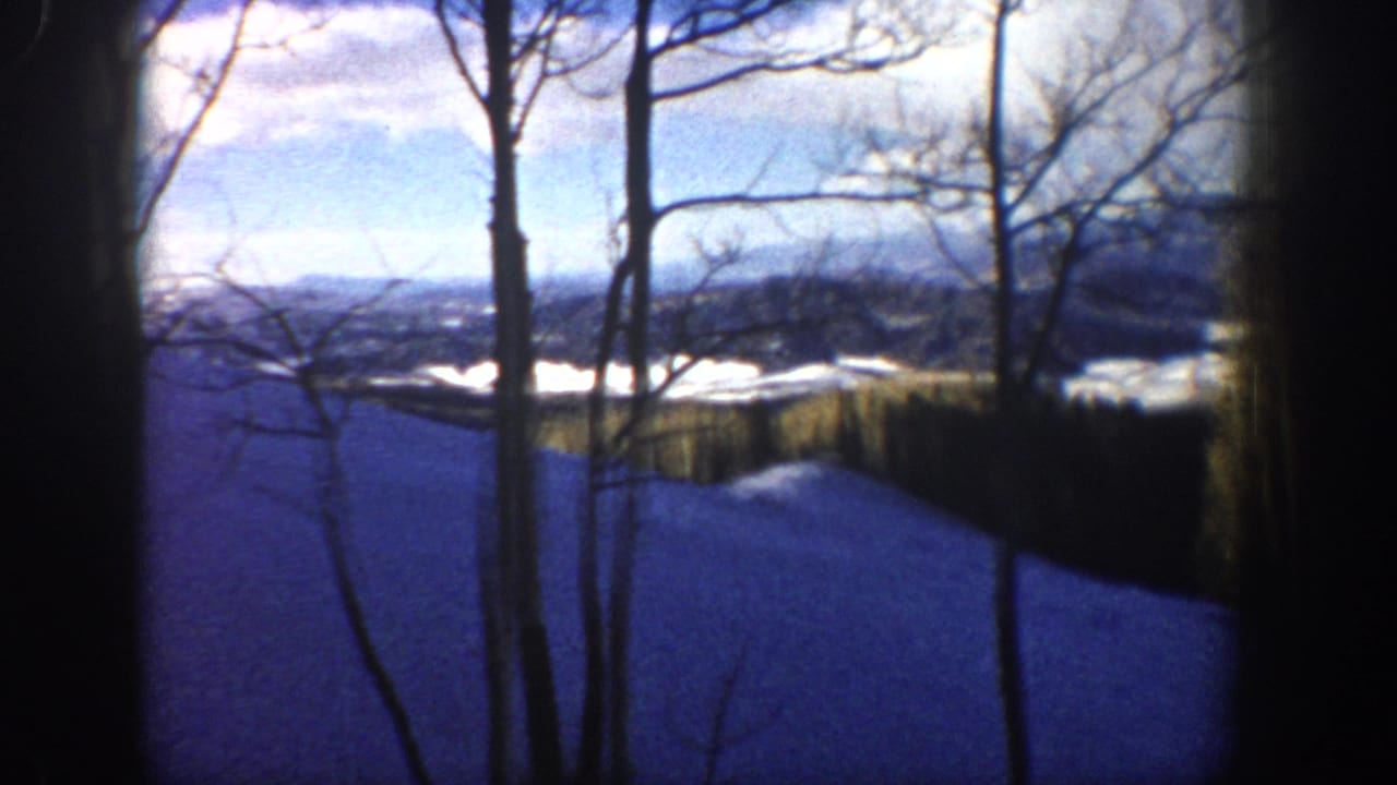 Aspen, Colorado winter vista from 1961 8mm footage, with bare trees silhouetted over snow and distant ridges.