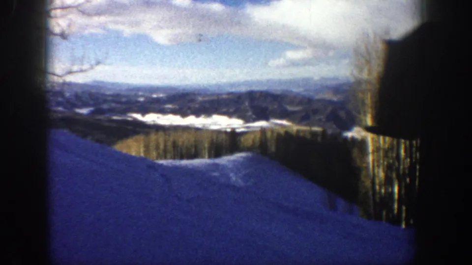 Aspen, Colorado 8mm frame showing a snowy foreground slope, far ridges, pale clouds, and a dark vertical film-edge shape.