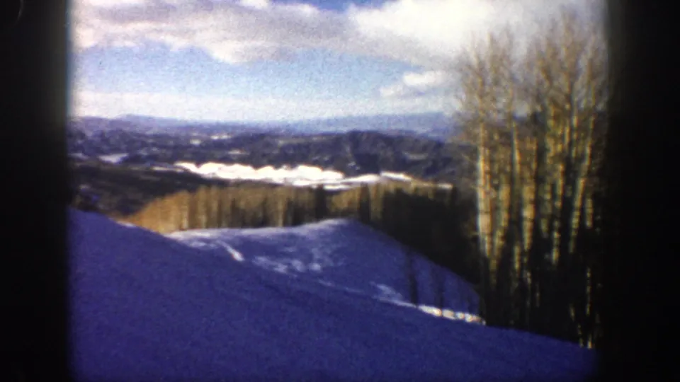 1961 Aspen, Colorado winter scene with snow in the foreground, bare aspen trees at right, ridges beyond, and bright sky.