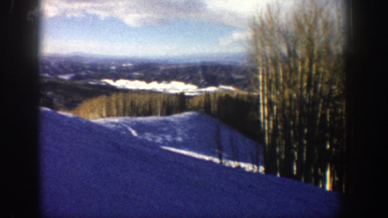 1961 Aspen, Colorado home-movie frame showing a snowy slope, bare aspen trees, distant mountains, and blue winter shadows.