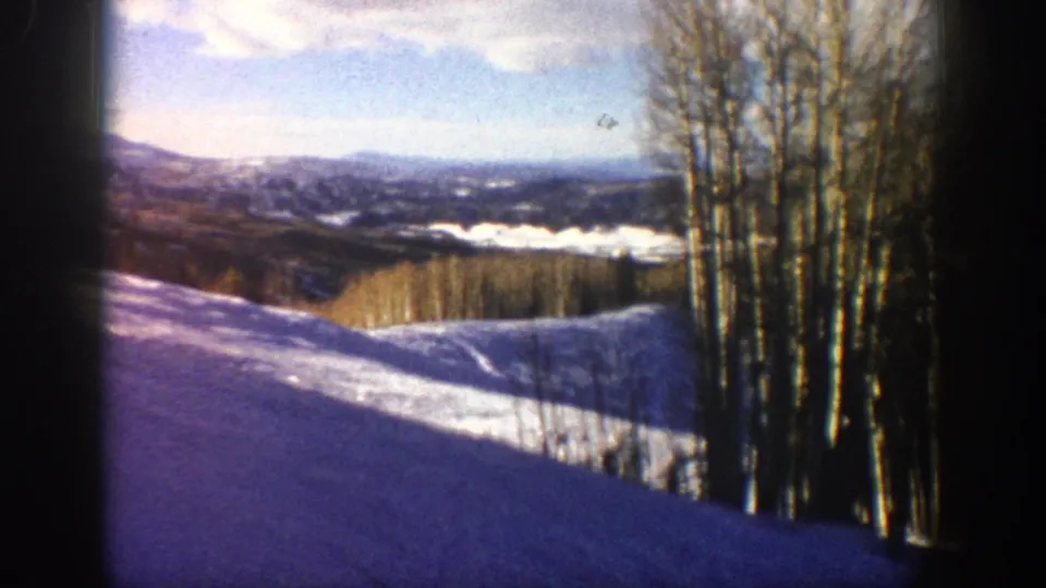 1961 Aspen-area home-movie frame showing a snow-covered overlook, bare aspen trunks, distant hills, and visible 8mm film grain.