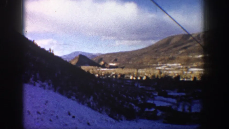 1961 Aspen, Colorado 8mm still showing a blue-purple tinted snowy hillside above a mountain valley with buildings and layered hills in the distance.