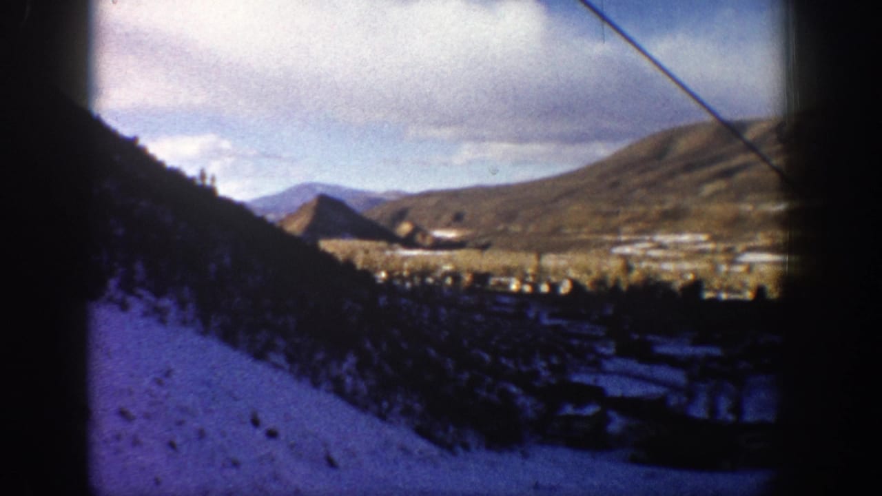 1961 Aspen home-movie view of a snowy forested slope and distant mountain valley, with a cable crossing the frame.