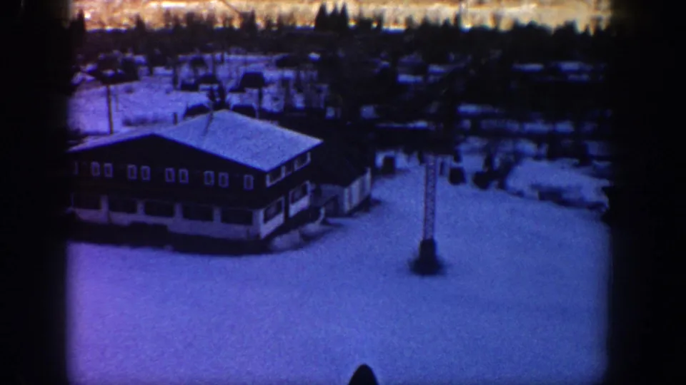 1961 Aspen resort footage shows a chalet-style lodge roof, lift tower, snowfield, and dark tree line from an elevated angle.
