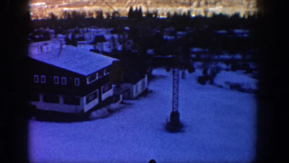 Elevated 1961 Aspen view of a snow-covered lodge and nearby tower, recorded with grainy blue 8mm home-movie texture.