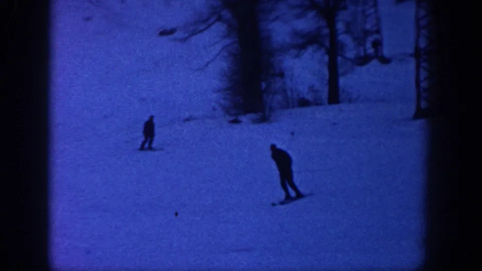 1961 Aspen frame with one nearer skier leaning downhill and another smaller skier farther back on the snow.