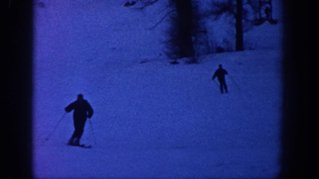 Two skiers appear as dark silhouettes on a snowy Aspen, Colorado slope in blue low-light 8mm footage from the supplied 1961 metadata.