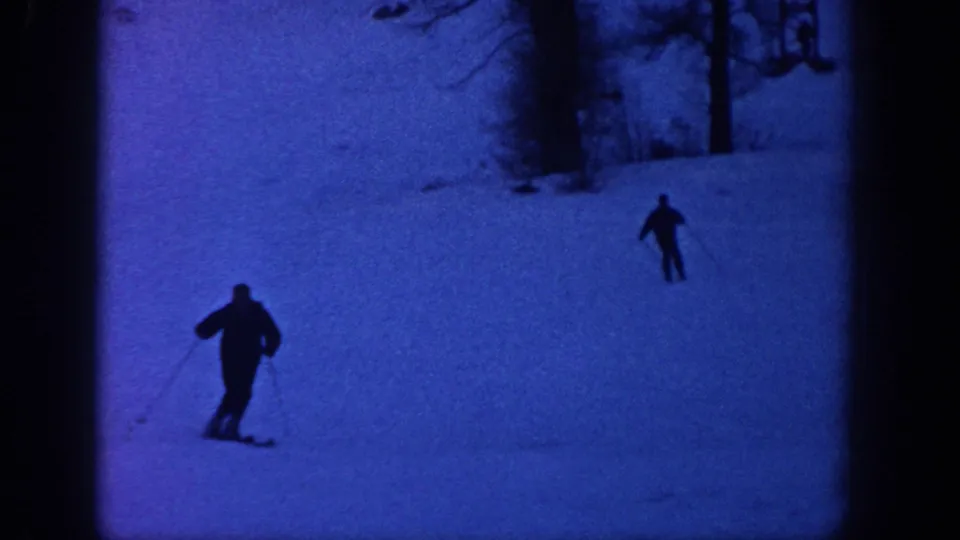 Two skiers appear as dark silhouettes on a snowy Aspen, Colorado slope in blue low-light 8mm footage from the supplied 1961 metadata.
