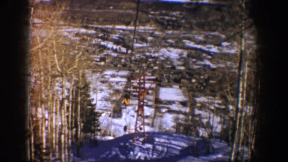 1961 Aspen frame with the lift cable passing a red tower over snow, trees, and a small distant rider or skier shape.