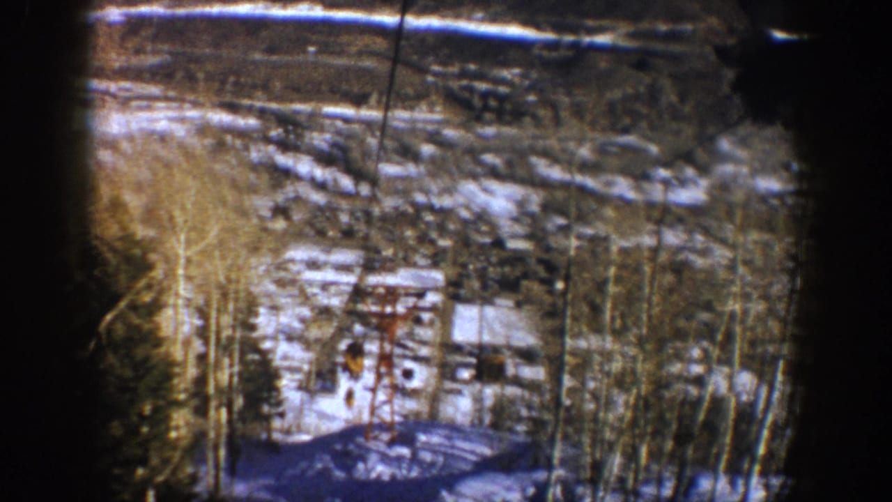 Ski-lift structure and cables above a patchy snowy valley framed by dark film edges.