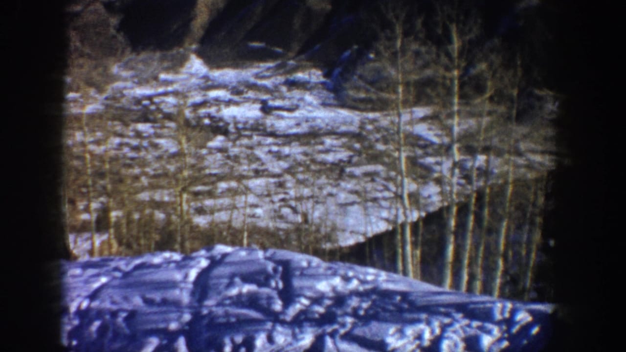 1961 Aspen home-movie frame showing a snow-covered slope, bare aspen trees, and rocky mountain terrain within visible 8mm gate edges.