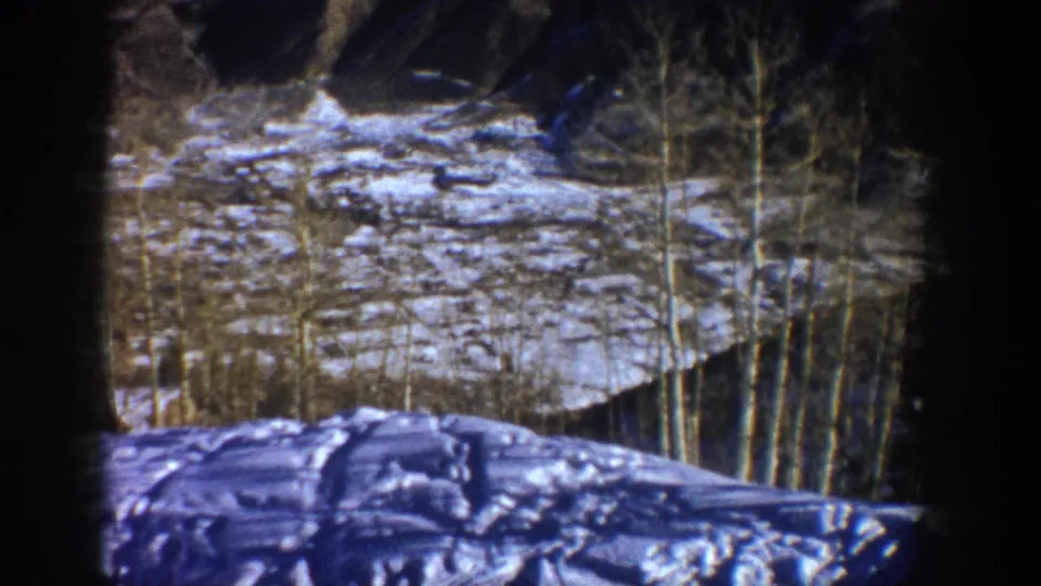 1961 Aspen home-movie frame showing a snow-covered slope, bare aspen trees, and rocky mountain terrain within visible 8mm gate edges.