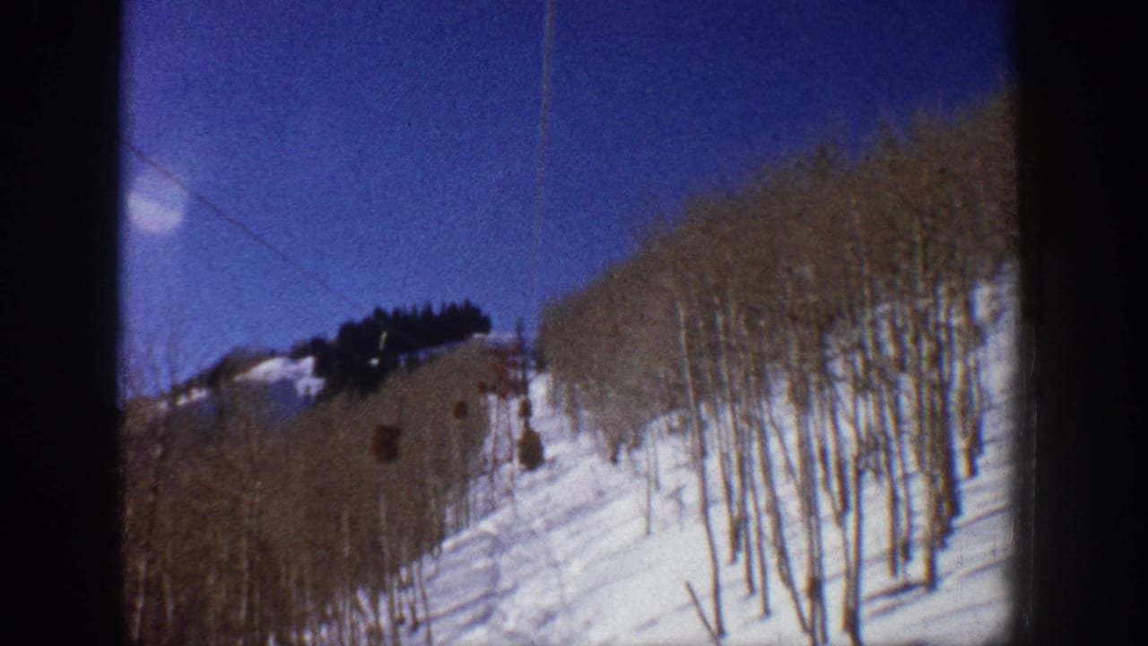 1961 Aspen ski-lift view over a snowy slope lined with bare aspen trees under a deep blue sky.