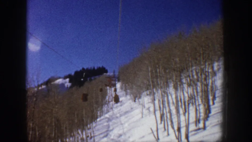 1961 Aspen ski-lift view over a snowy slope lined with bare aspen trees under a deep blue sky.