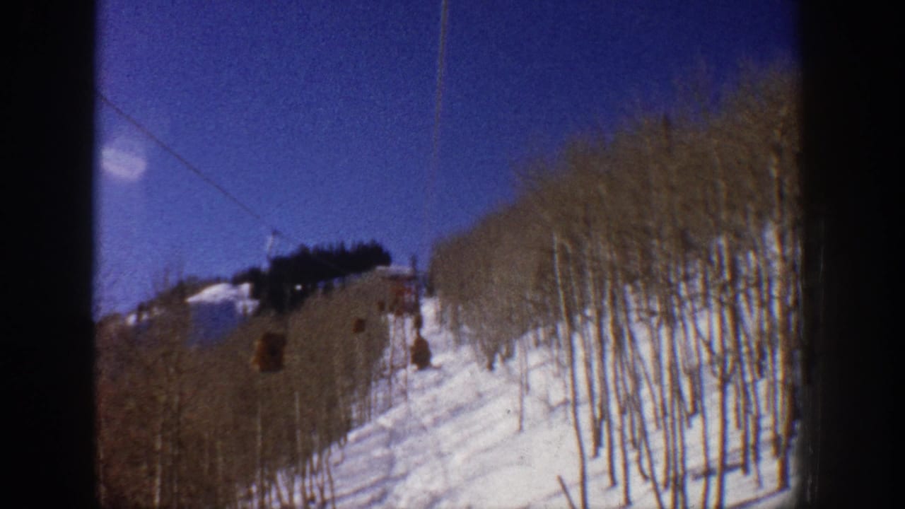 Vintage Aspen, Colorado ski-lift view showing chairs moving above a snowy run and leafless aspen grove.