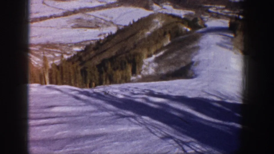 Aspen home-movie frame from 1961 showing a snowy ski slope, wooded ridge, distant hills, and blue winter sky.