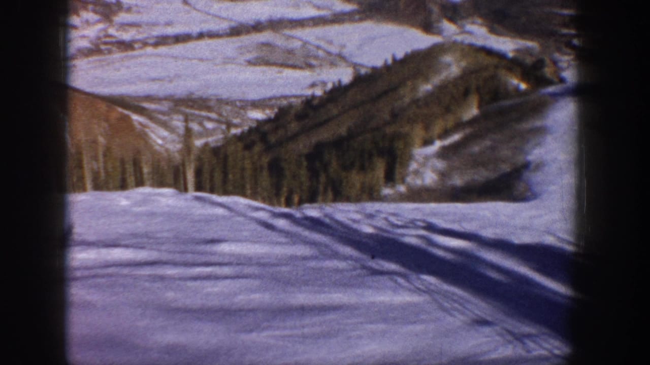 1961 Aspen-area 8mm frame showing a snowy slope, wooded hillside, distant mountains, and a lone small figure crossing the snow.