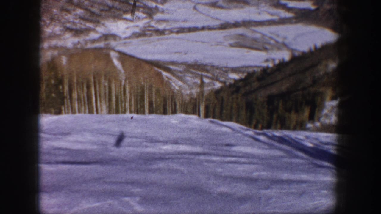 Snow-covered foreground with trees, distant ridges, and a small figure near the center.