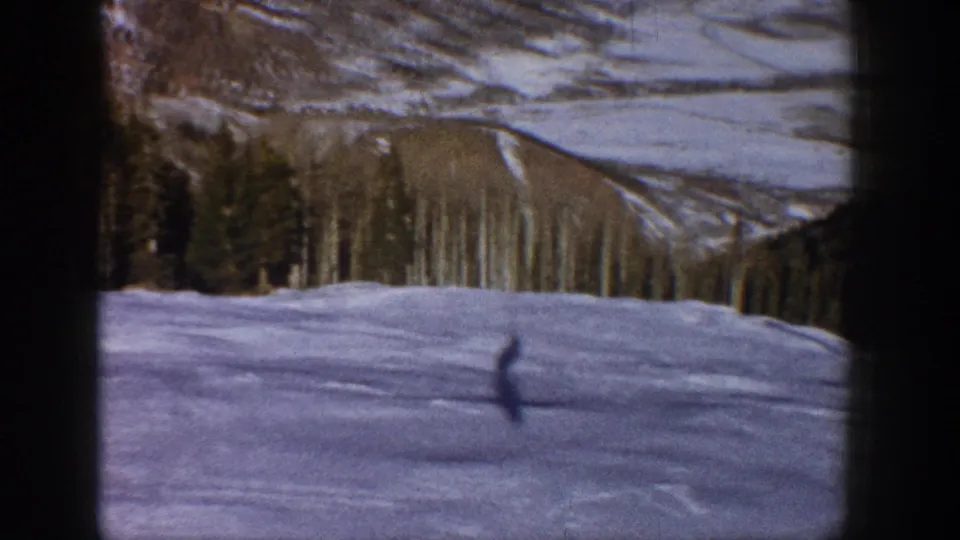 1961 Aspen-area home-movie frame showing a lone dark figure moving over snow in front of aspen and evergreen trees.