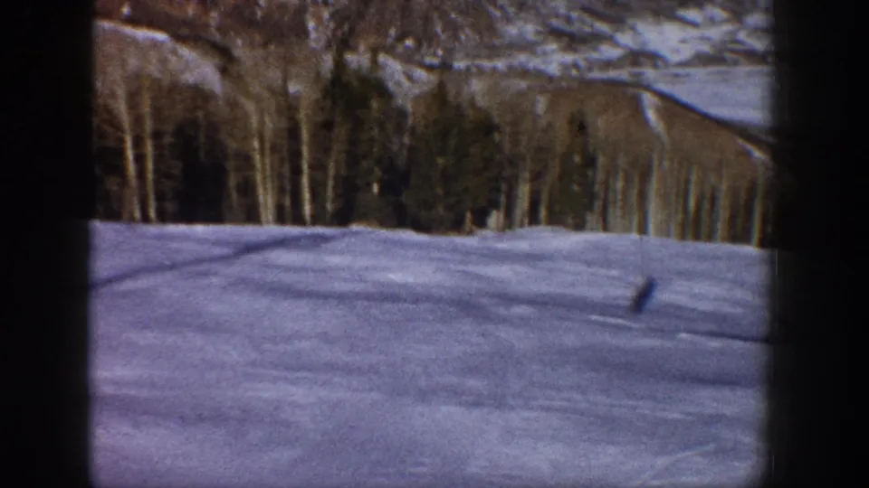 1961 Aspen, Colorado 8mm frame showing a small figure on snow, backed by trees and distant winter mountain terrain.