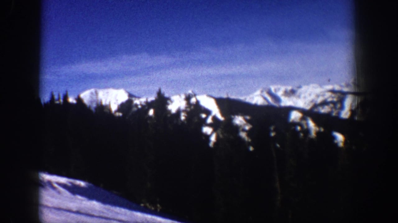 1961 Aspen, Colorado 8mm frame showing snow-covered mountain ridges, evergreen tree silhouettes, and a bright winter sky.