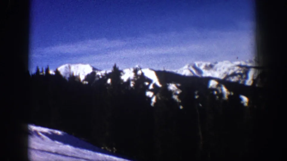 1961 Aspen, Colorado 8mm frame showing snow-covered mountain ridges, evergreen tree silhouettes, and a bright winter sky.