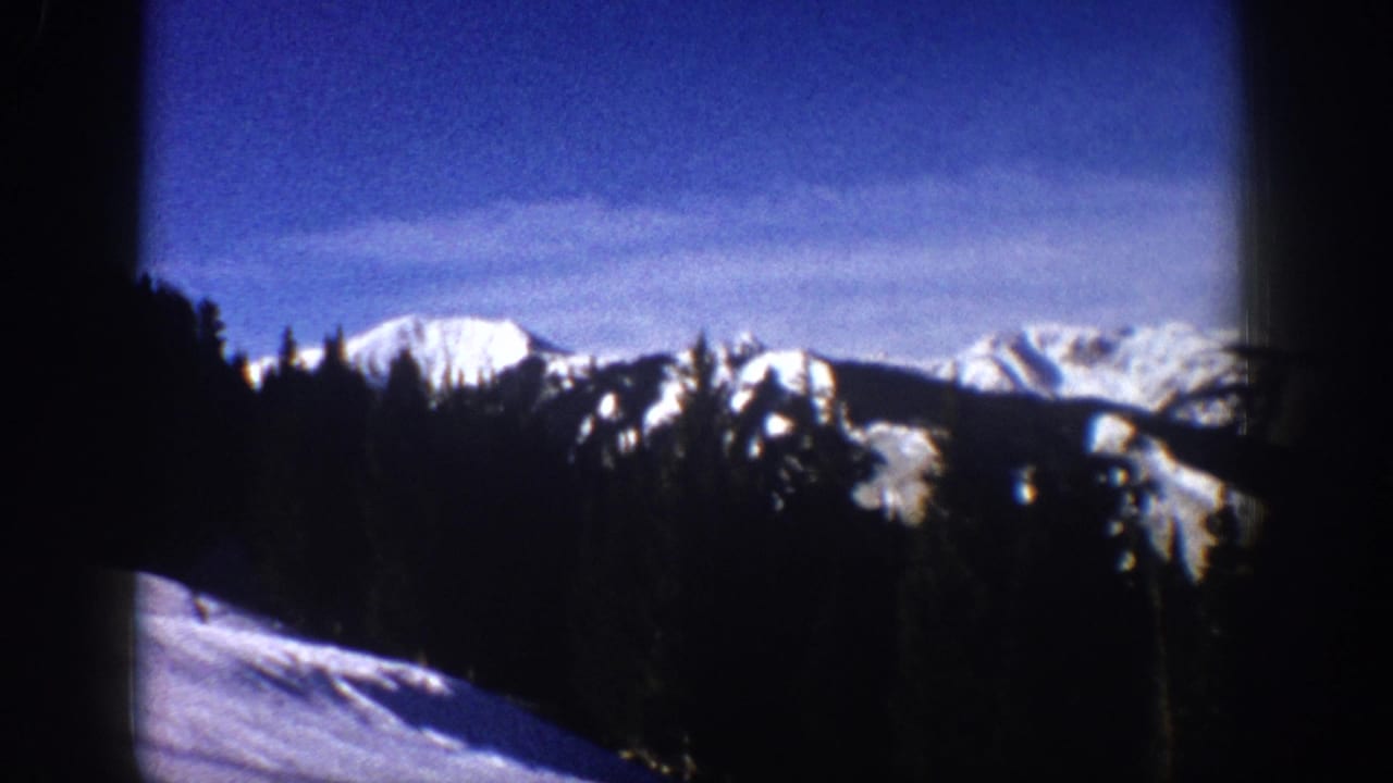Distant snow peaks and trees with a bright snowy slope in front.