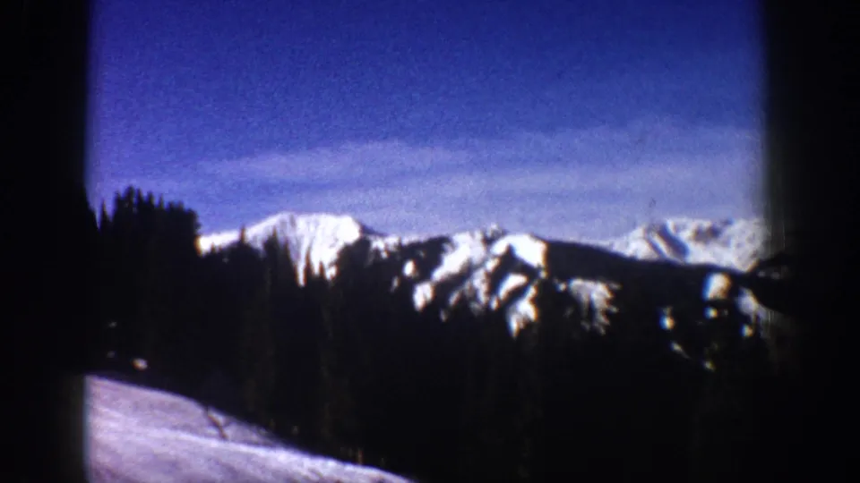 1961 Aspen, Colorado frame showing a snow-covered ridgeline, shadowed evergreen trees, and a pale snowy slope in front.