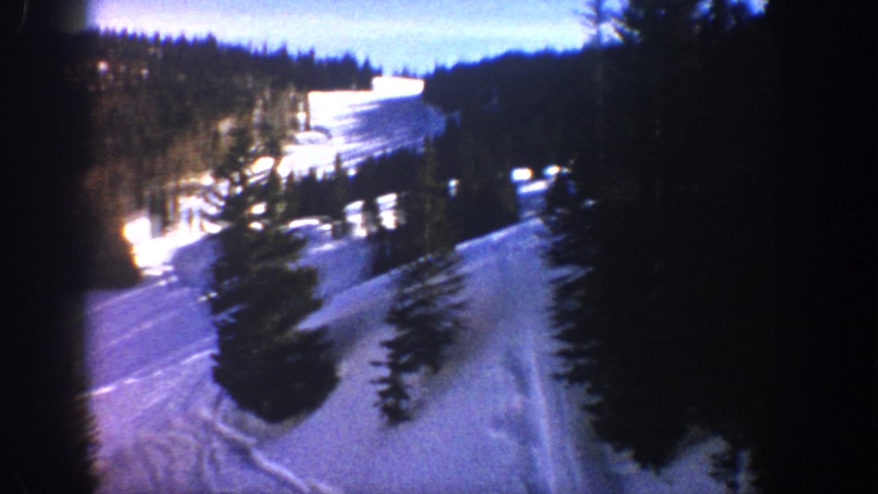Snowy mountain run with dark evergreens and a bright distant structure.