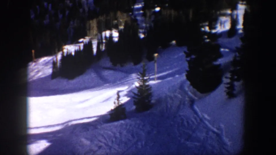 1961 Aspen winter frame showing a snow run, dark evergreens, and a small pole or sign beside the slope.