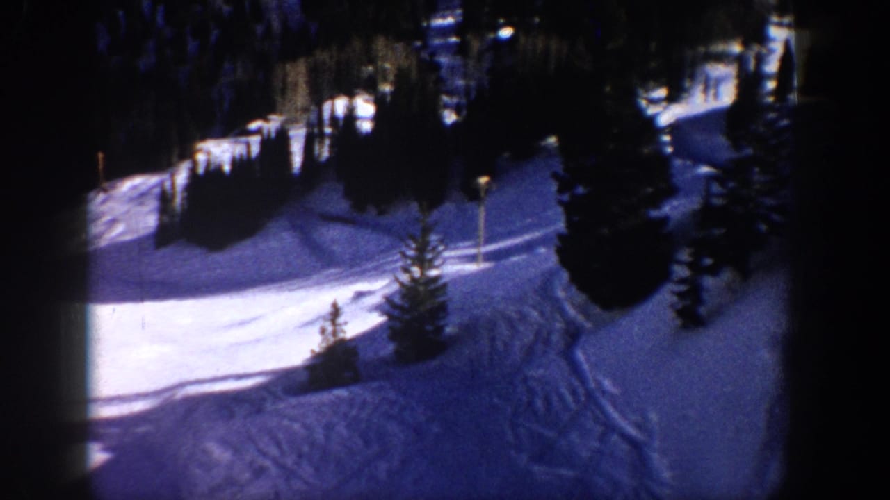 1961 Aspen home-movie frame showing a snow-covered slope, evergreen trees, and faint tracks in a winter resort landscape.