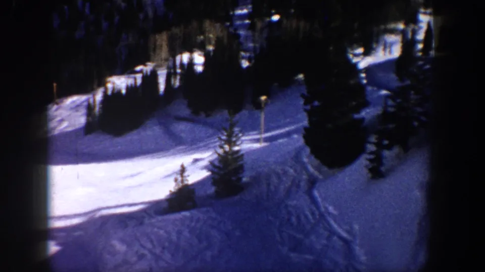 1961 Aspen home-movie frame showing a snow-covered slope, evergreen trees, and faint tracks in a winter resort landscape.