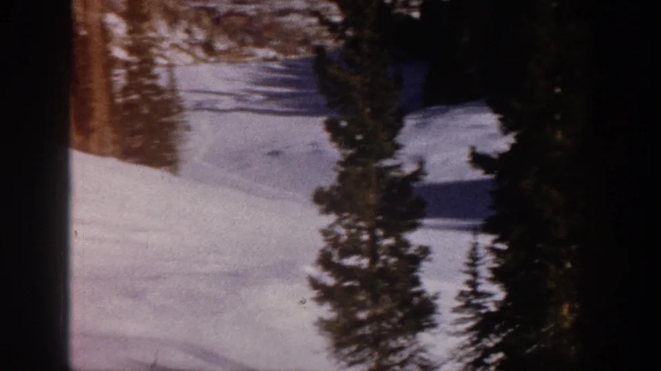 1961 Aspen frame with a snowy ski slope, tall evergreen trees, soft shadows, and warm color shift from the 8mm scan.