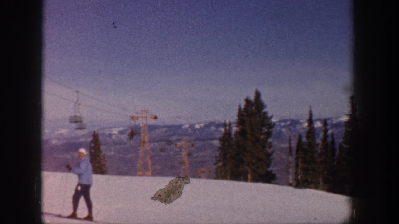 1961 Aspen home-movie frame showing a skier in a light blue jacket on a snowy slope with lift towers, trees, and mountains behind.