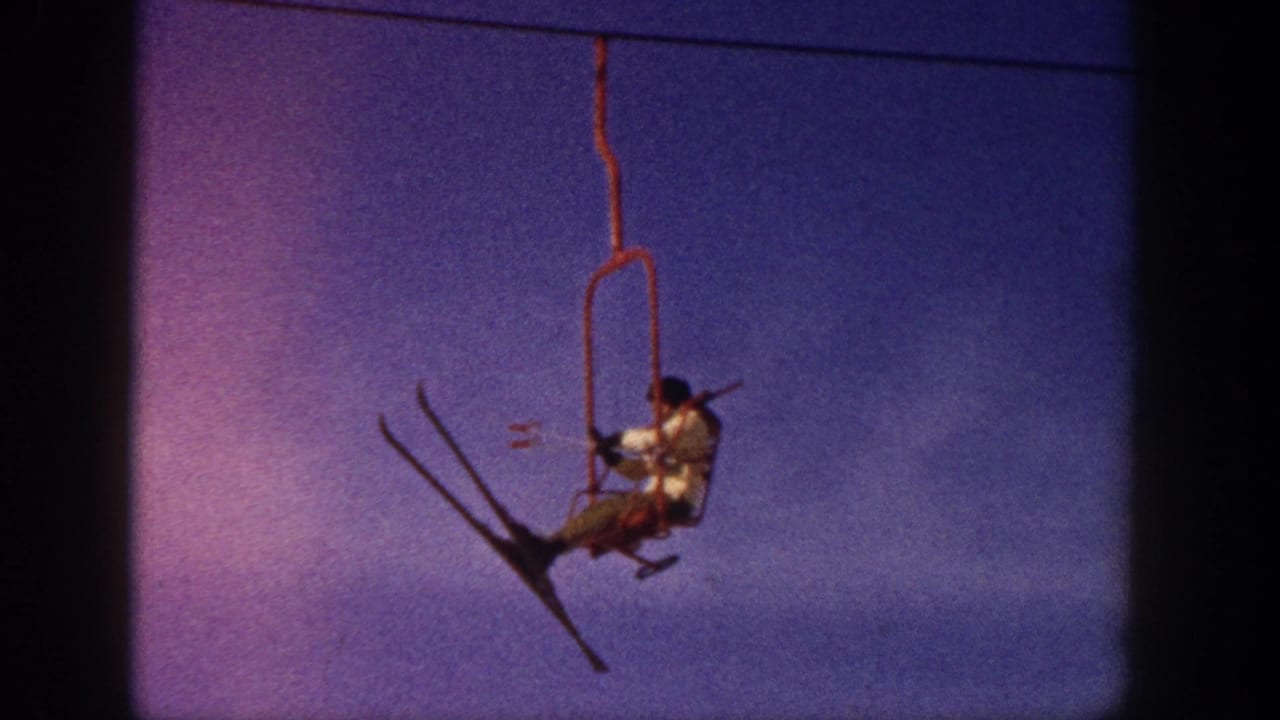 In supplied 1961 Aspen footage, a skier in a light jacket sits on a red chairlift against a purple-blue sky.