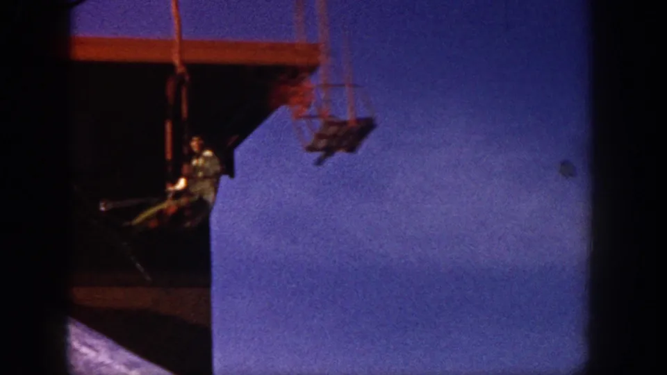 The chairlift rider nears a dark support structure, with another lift chair partly visible in the background.