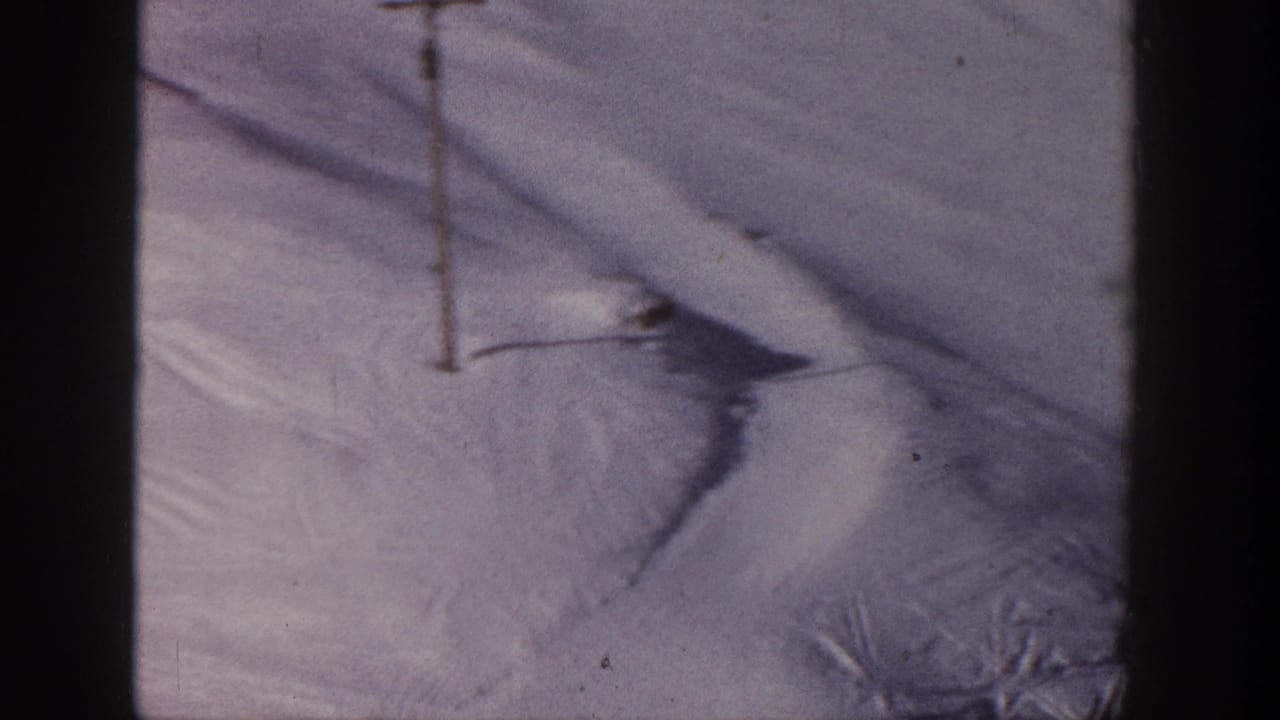 1961 Aspen home-movie frame showing a snow-covered ski slope with a single lift pole and visible tracks in the snow.