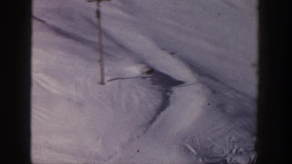 1961 Aspen home-movie frame showing a snow-covered ski slope with a single lift pole and visible tracks in the snow.