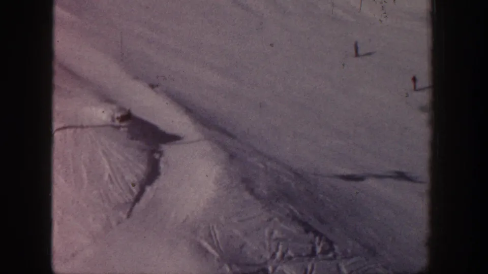 Aspen 1961 home-movie view of a snow-covered ski run with lift hardware and tiny distant skier figures or marks on the slope.